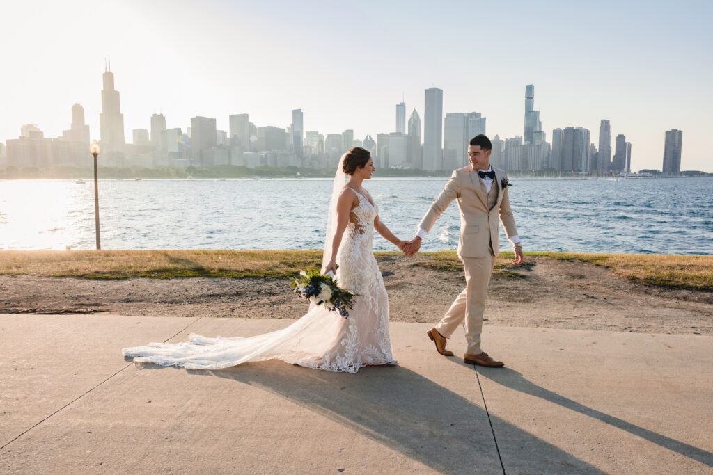 Groom in tan suit holds hands with his bride at museum campus in Chicago, IL