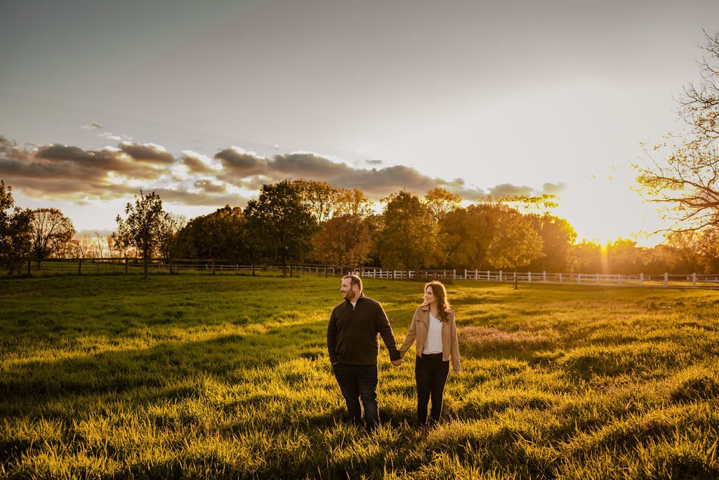 A couple hold hands while standing in a field at sunset at Danada House.