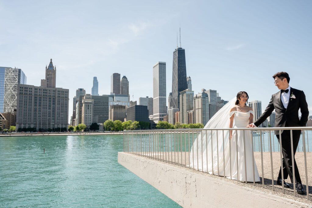 Bride and groom hold hands in front of the Chicago skyline at Milton Lee Olive Park in Chicago, IL.