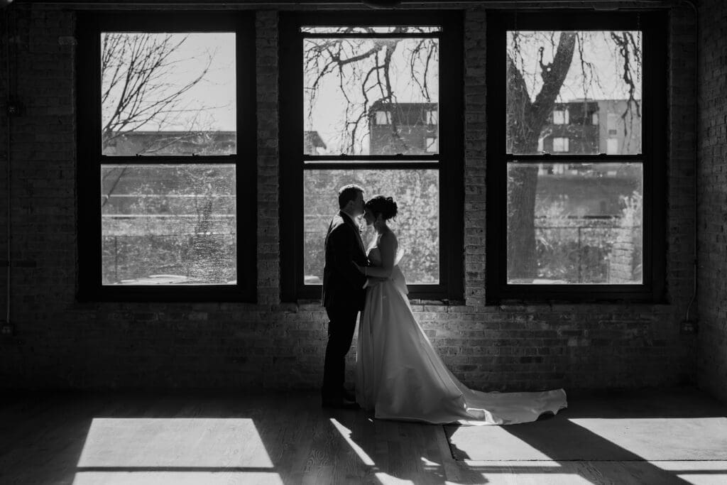 Bride and groom embrace in front of a window at Artifact Events in CHicago.