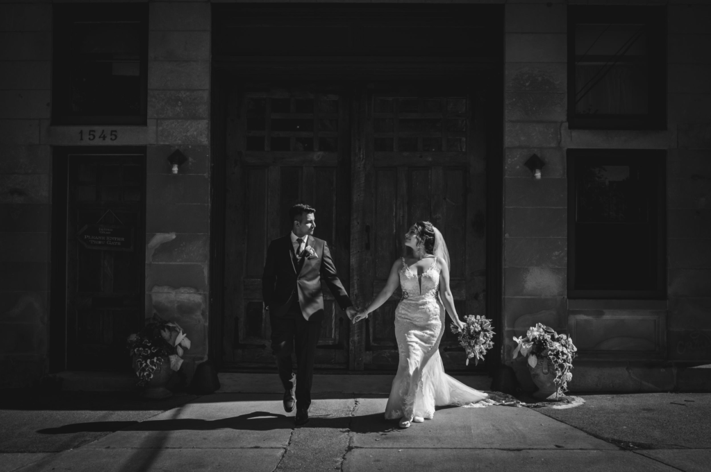 Bride and groom walk in front the the big doors at before their outside wedding ceremony at The Firehouse in Chicago.