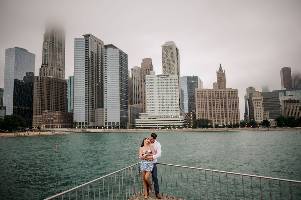 A couple embrace in front of the Chicago Skyline during their Chicago engagement session.