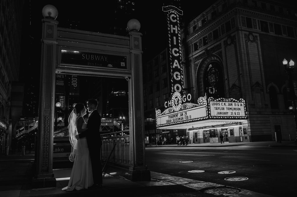 Bride and groom stand in front of he Chicago Theater at night. 