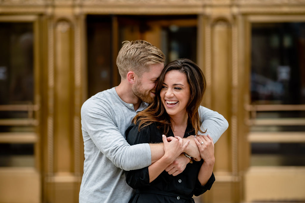 Man hugs women from behind in front of a gold door