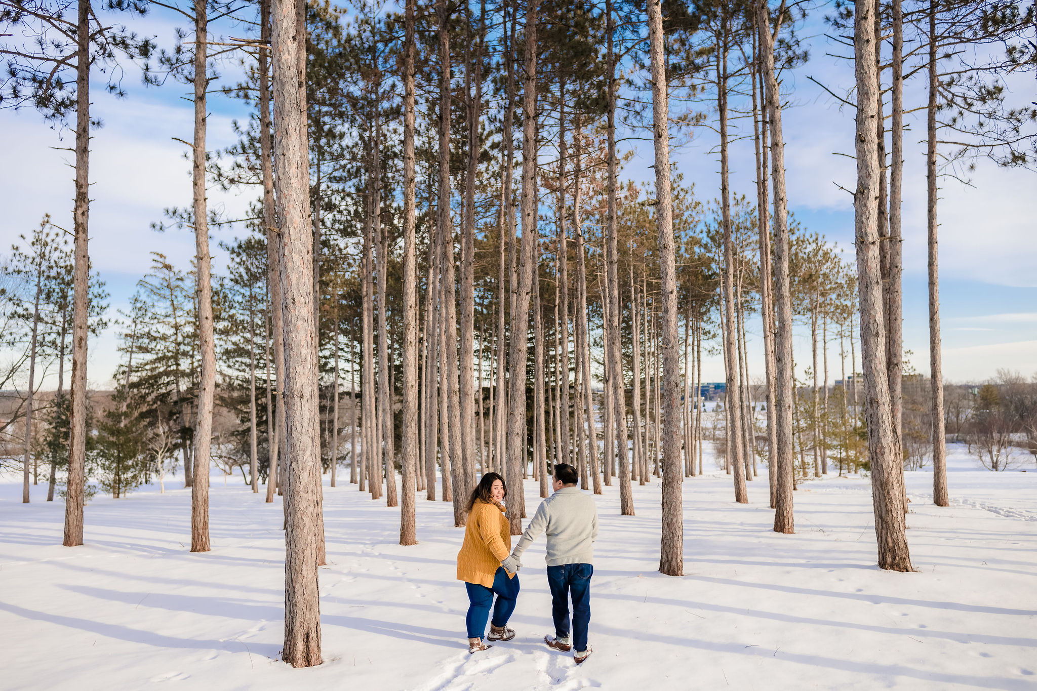 A couple walking in the snow surrounded by spruce trees.