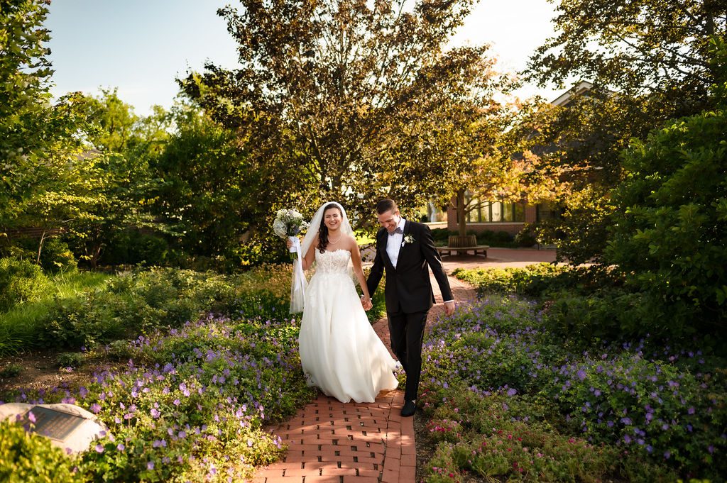 A bride and groom walk in the garden 
