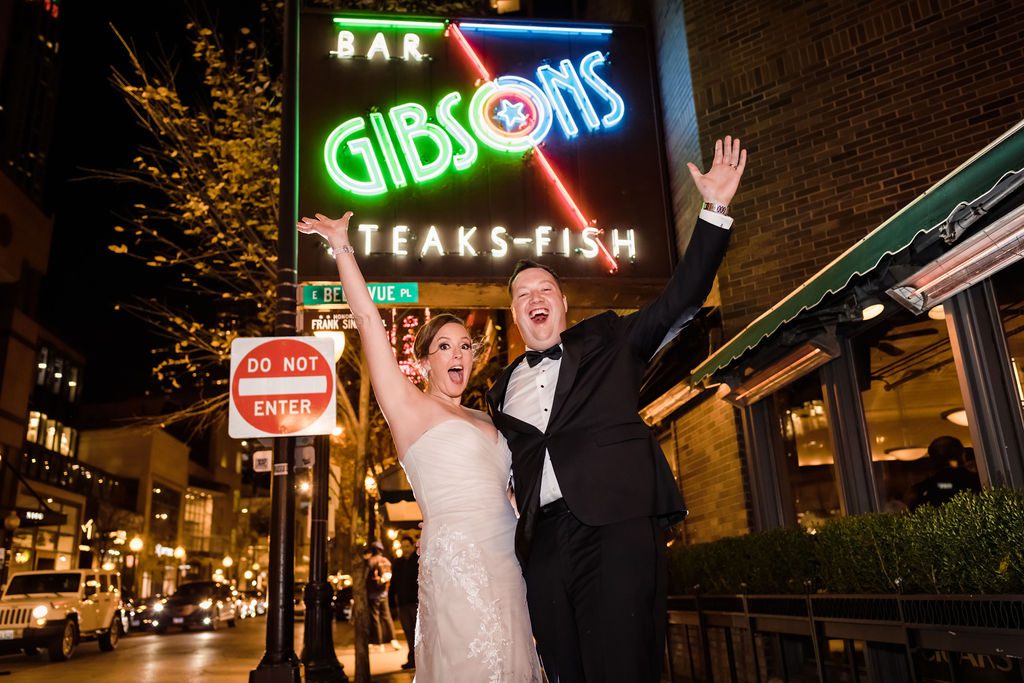 Bride and groom celebrate outside Gibsons Steakhouse in Chicago at night.