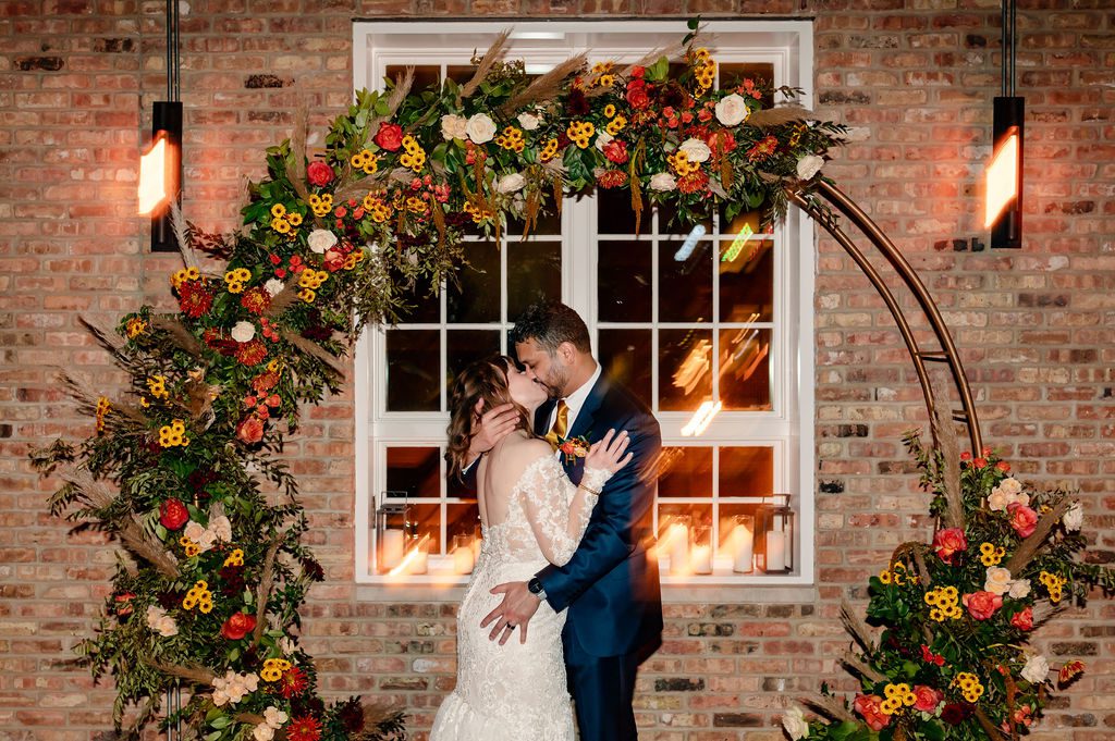 Bride and groom kiss in front of flower arch at Loft Lucia in Chicago, IL