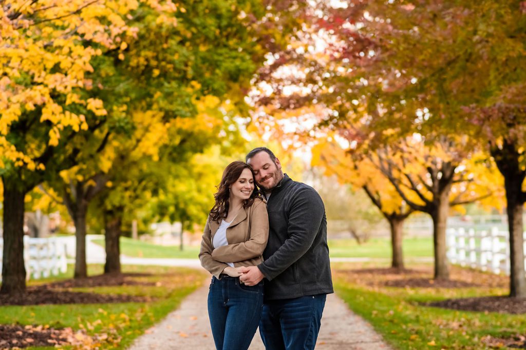 A couple embrace surrounded by fall trees at Danada House in Wheaton, IL