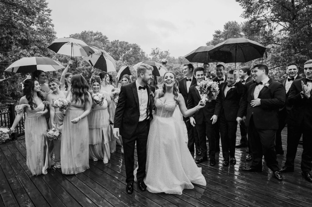 Bride and groom walk with their large wedding party in the rain
