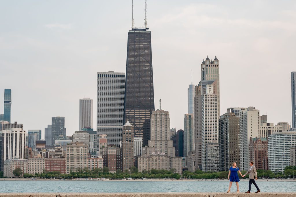 Couple hold hands while walking in front of the Chicago skyline at North Avenue Beach.