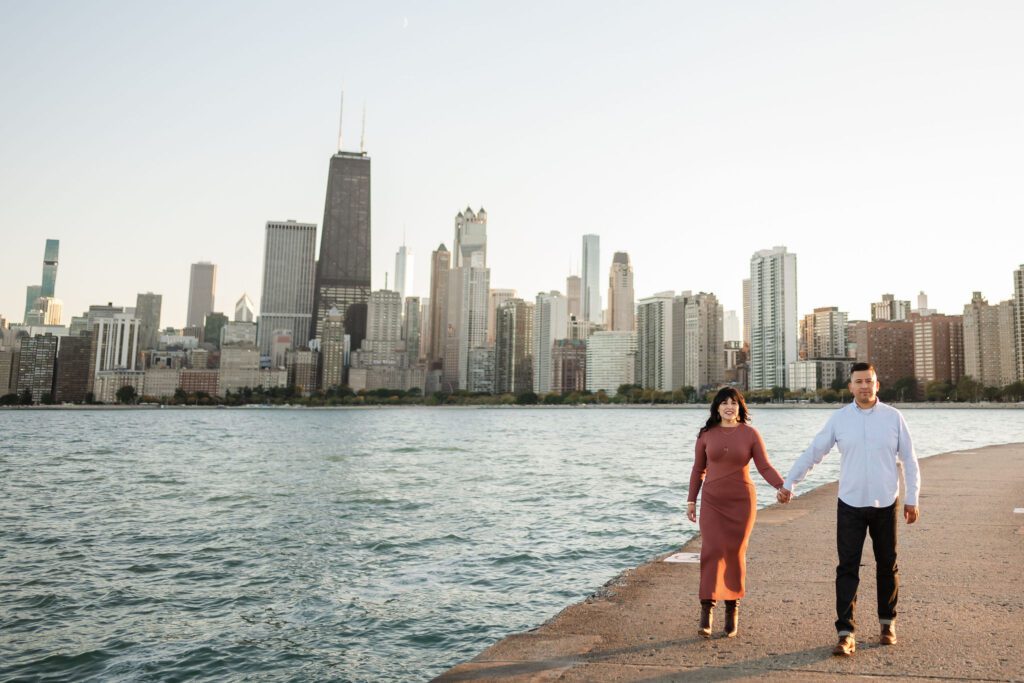 Women and man hold hands while walking at North Avenue Beach in Chicago with the skyline in the background. 