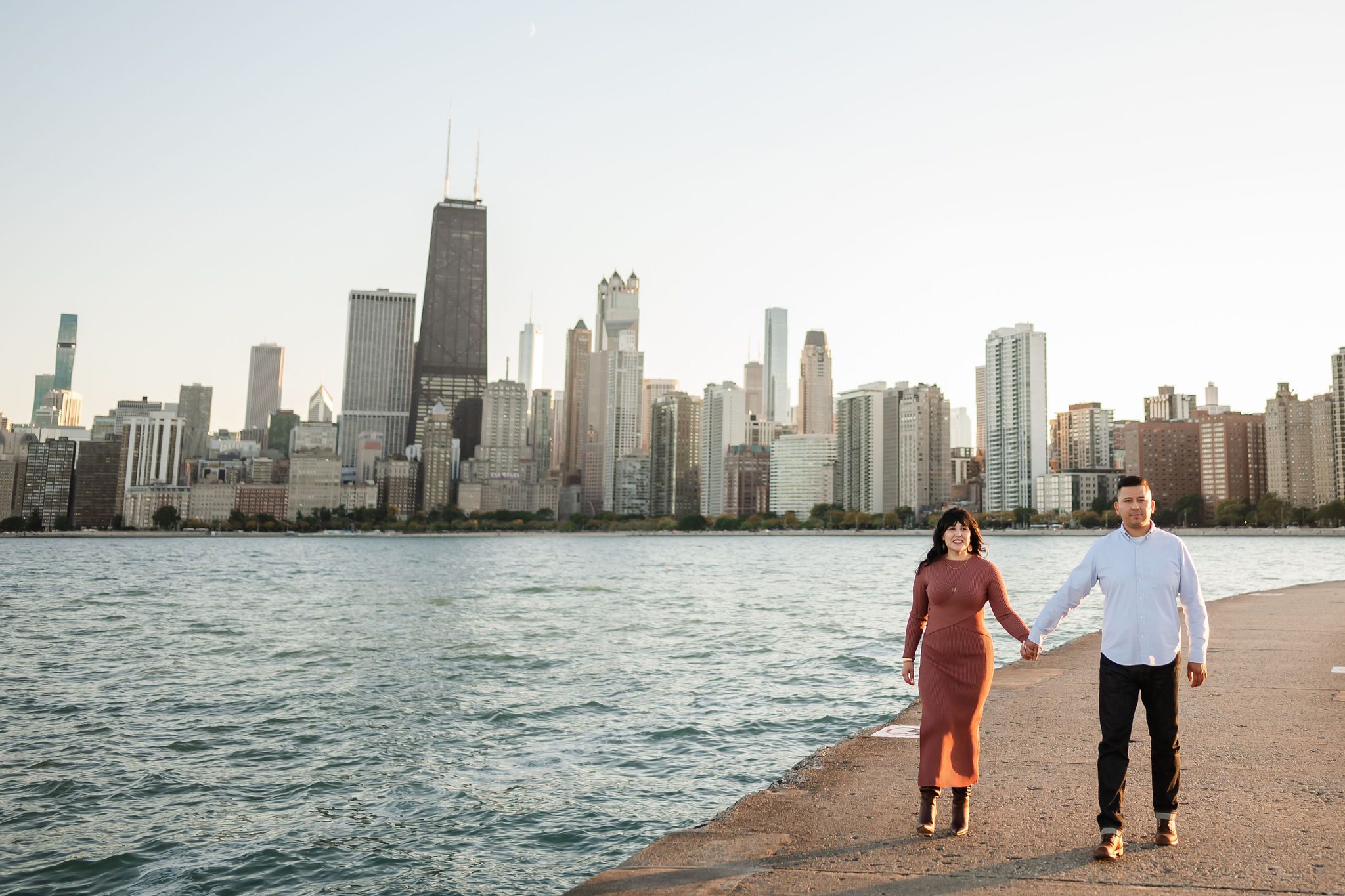 Women and man hold hands while walking at North Avenue Beach in Chicago with the skyline in the background.