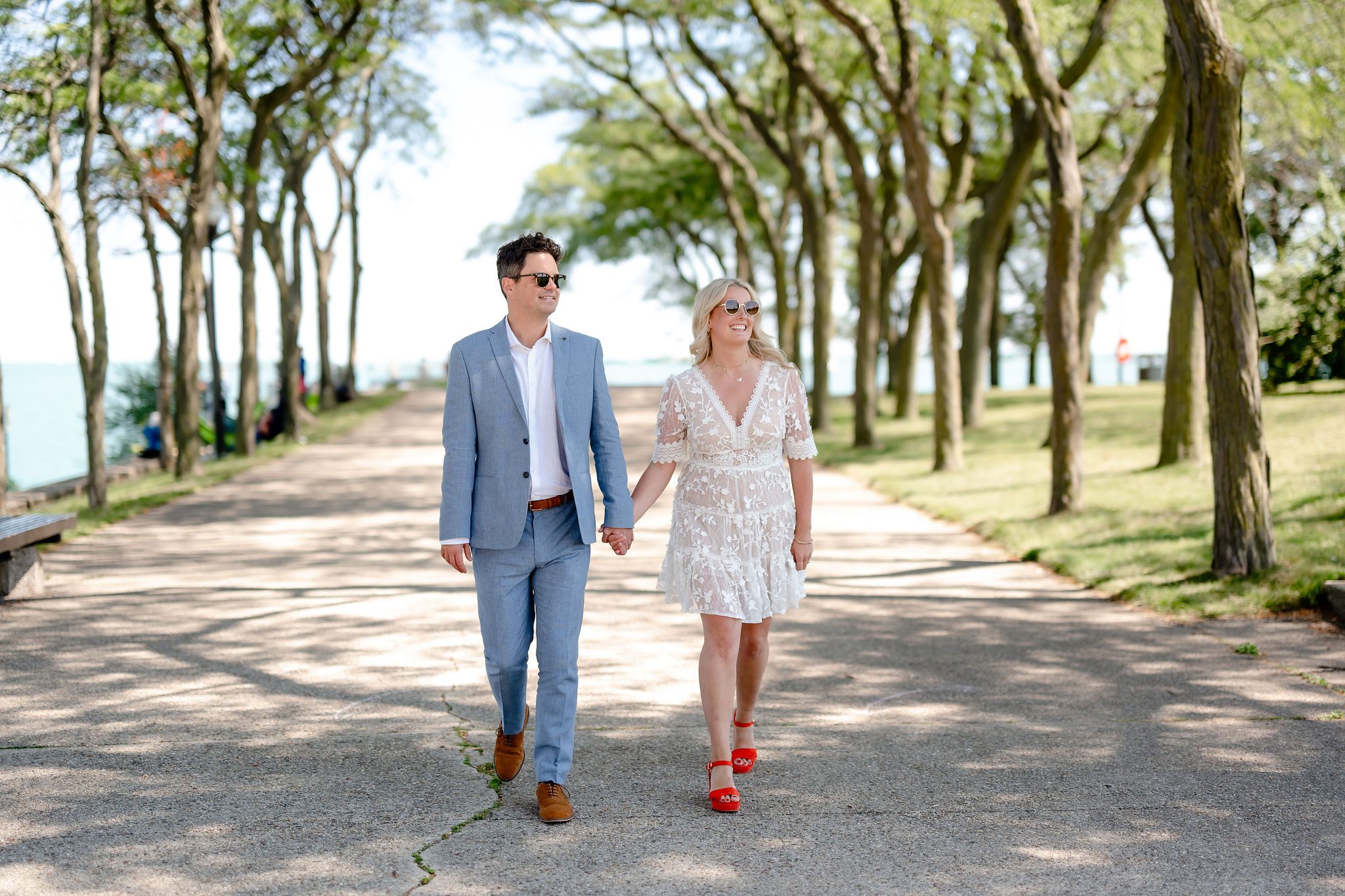 A couple wearing sunglasses walk down tree lined path at Milton Lee Olive Park in Chicago, IL