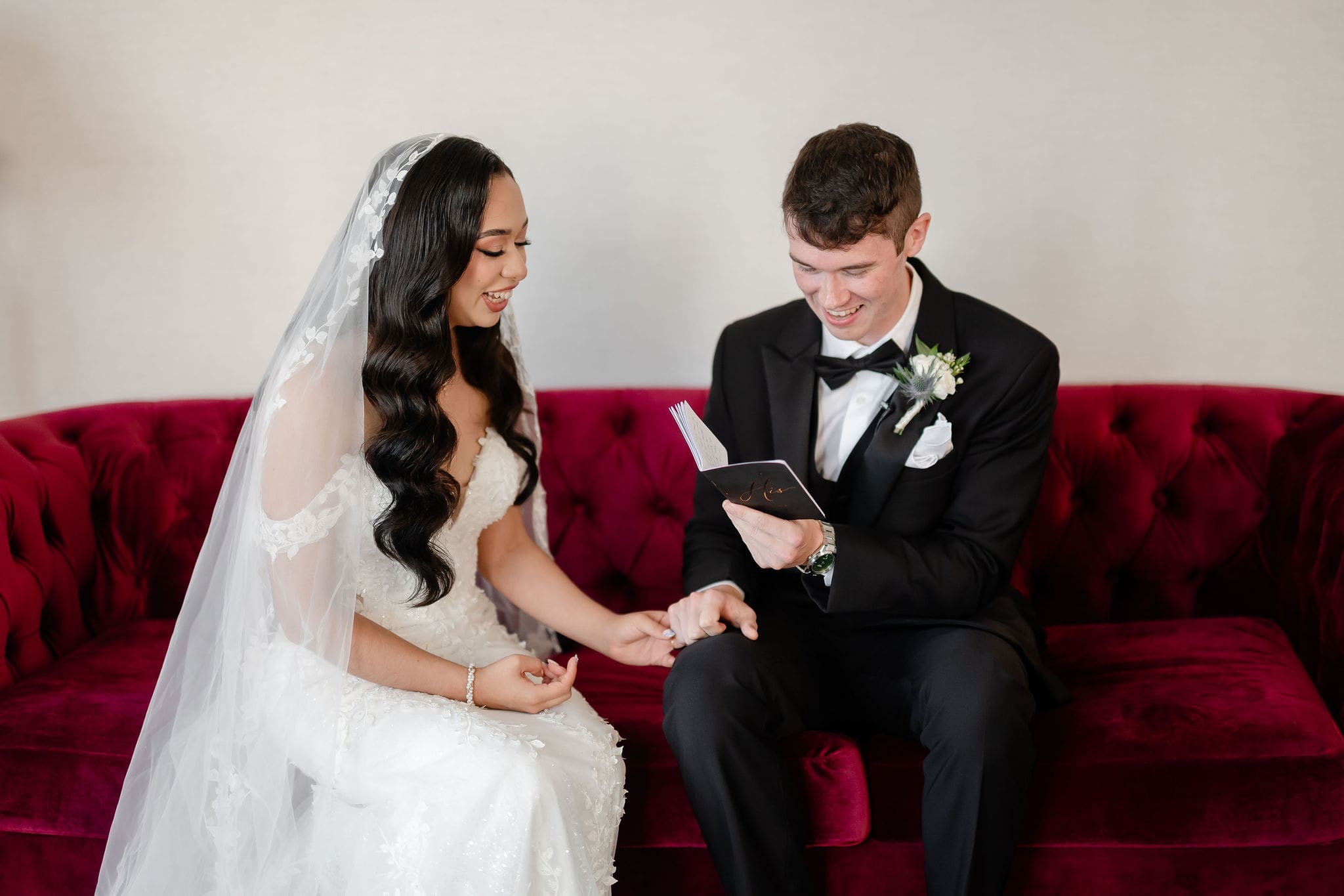 Bride and groom read private vows on a red couch