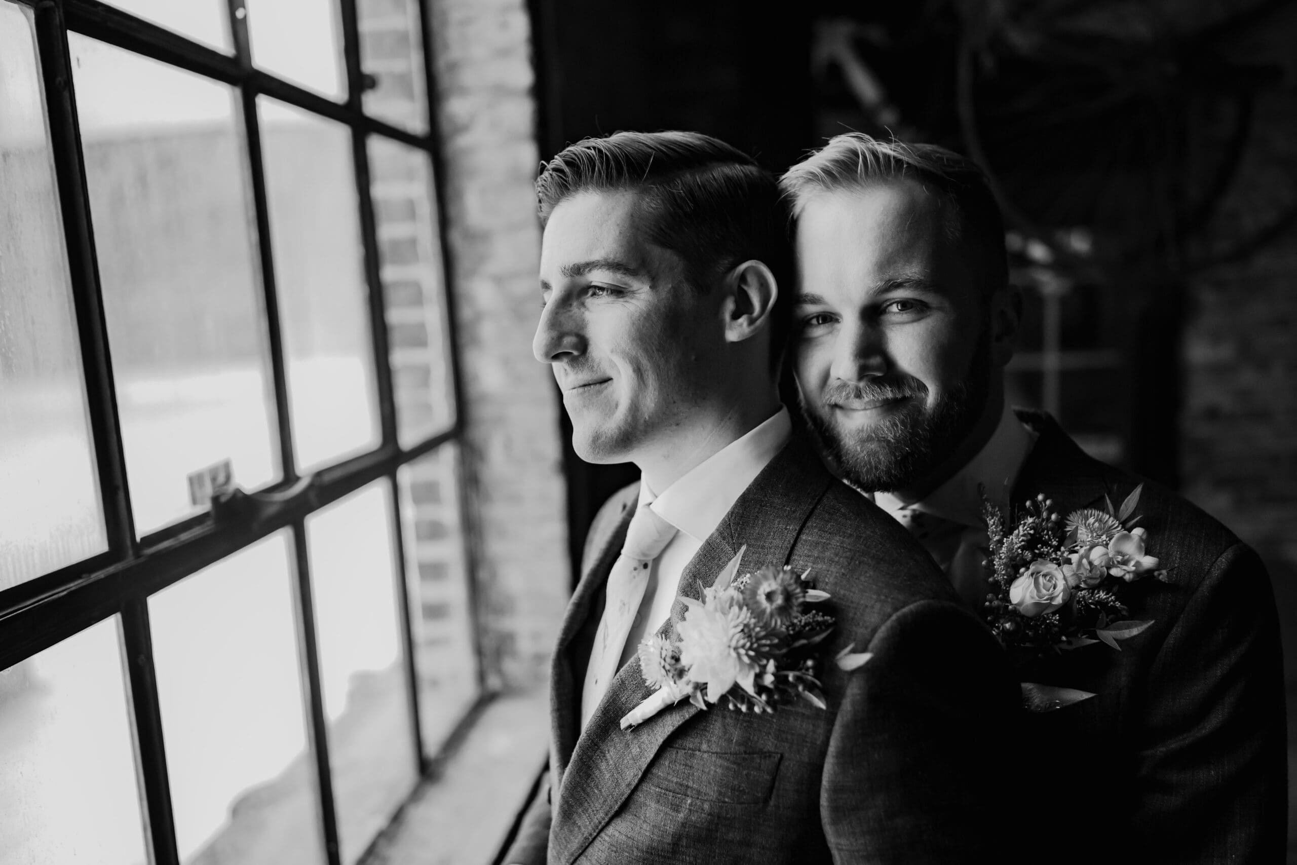 Two grooms embrace by a window before their Chicago wedding at Salvage One.