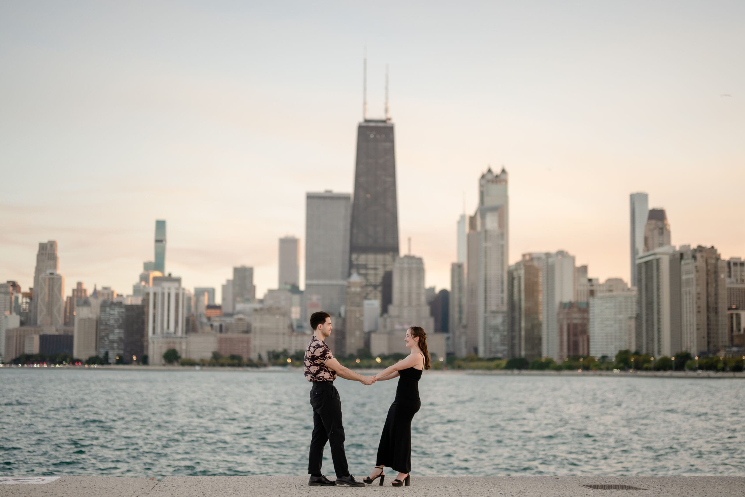 A couple faces each other and holds hands in front of the Chicago skyline at North Avenue Beach.