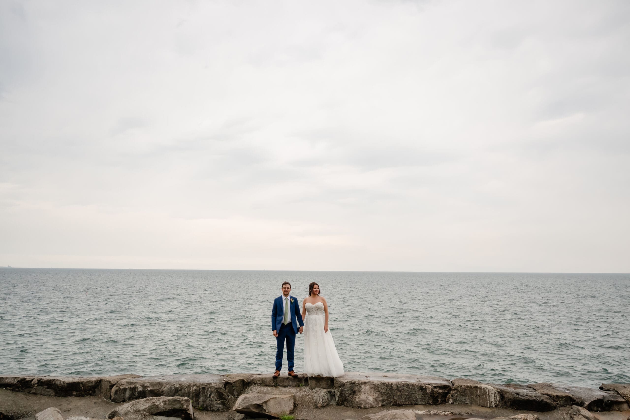 Bride and groom stand next to each other in front of Lake Michiagn